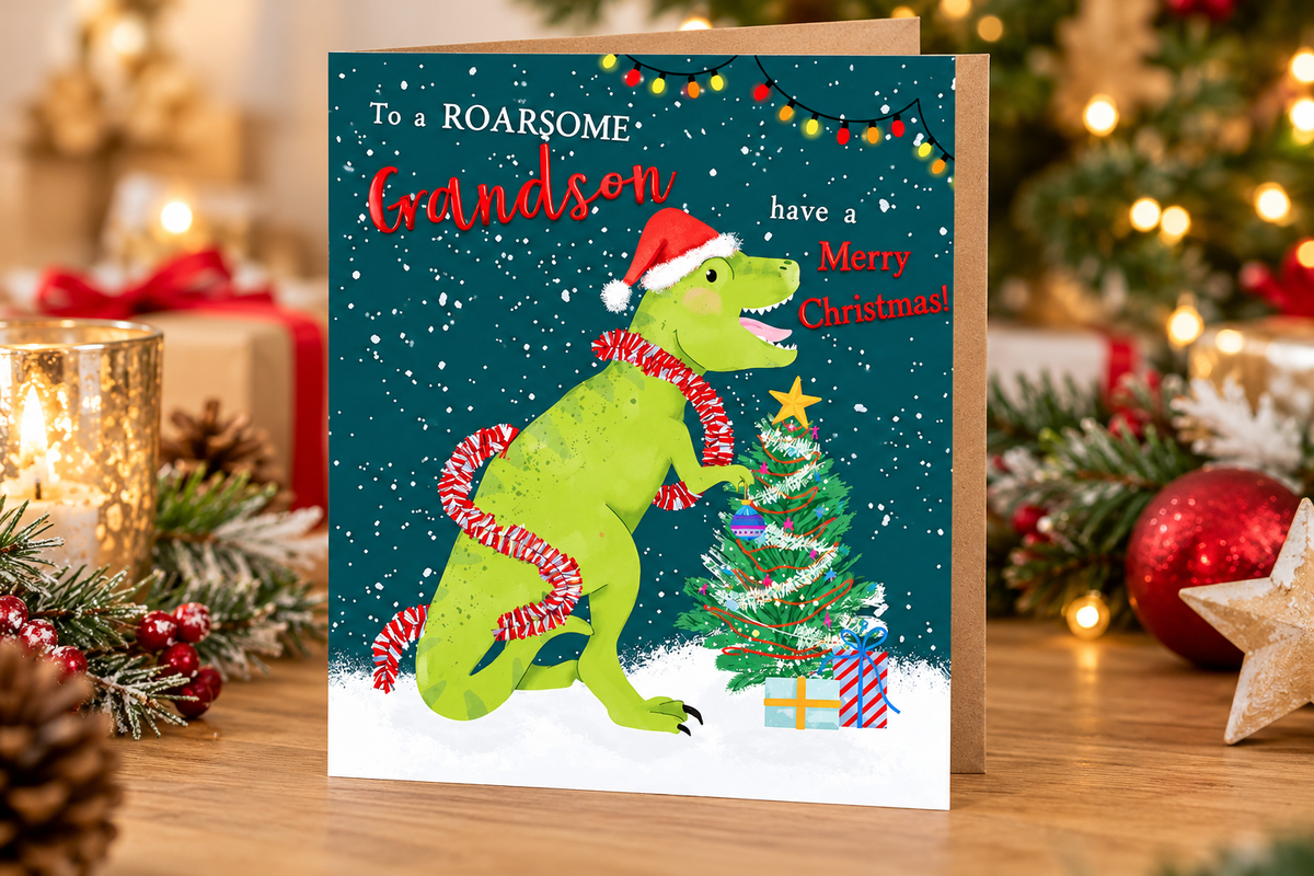 Roarsome Grandson dinosaur Christmas card displayed on wooden table with festive lights, gifts and decorations