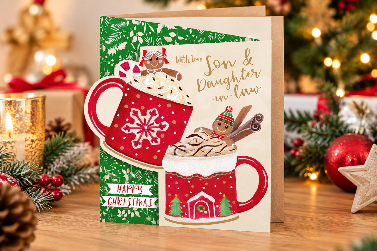 Son and Daughter-in-law hot chocolate Christmas card displayed on festive wooden table with candle, greenery and decorations