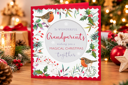 Grandparents robins and holly Christmas card standing on festive table beside candle and Christmas greenery