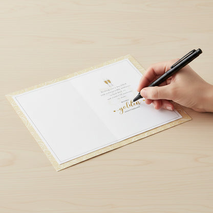 Made To Be Treasured golden wedding anniversary card with champagne glasses and heartfelt verse being signed by hand.