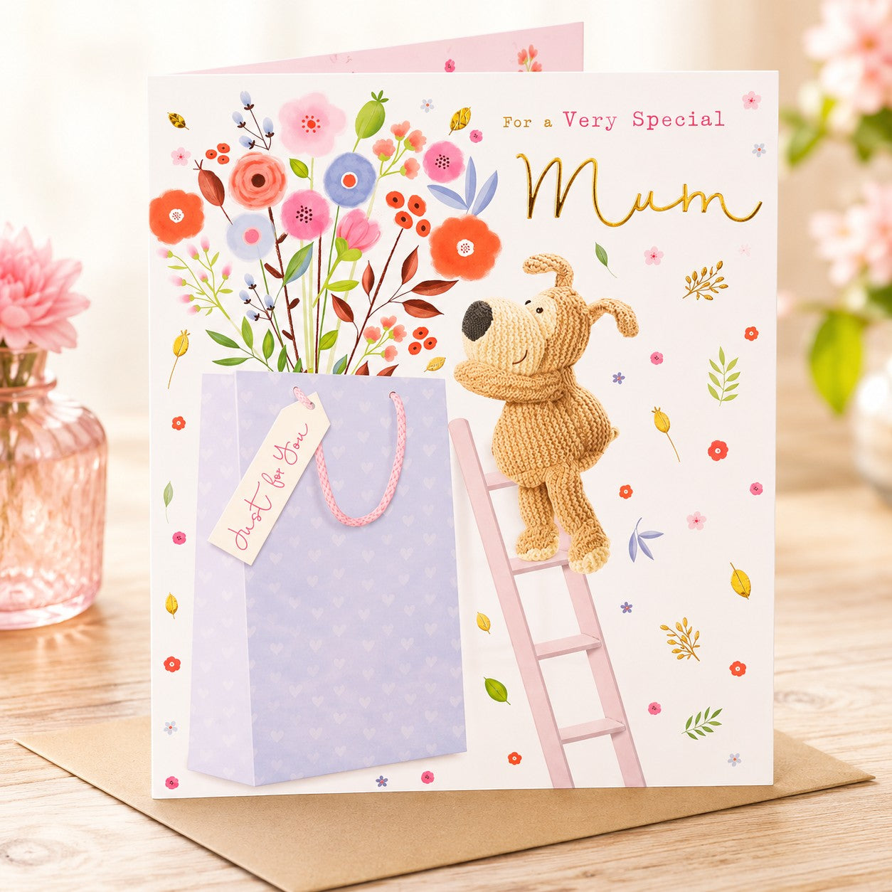 Made To Be Treasured birthday card for Mum featuring a knitted dog on a ladder next to a gift bag and floral design with gold foil details.