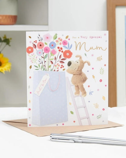 Made To Be Treasured Boofle birthday card for Mum, featuring a cute dog on a ladder reaching for flowers and a gift bag. Gold foil details.
