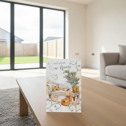 Made To Be Treasured Good Luck In Your New Home card with silver foil, featuring a sofa, boxes, and plant. Neutral tones.