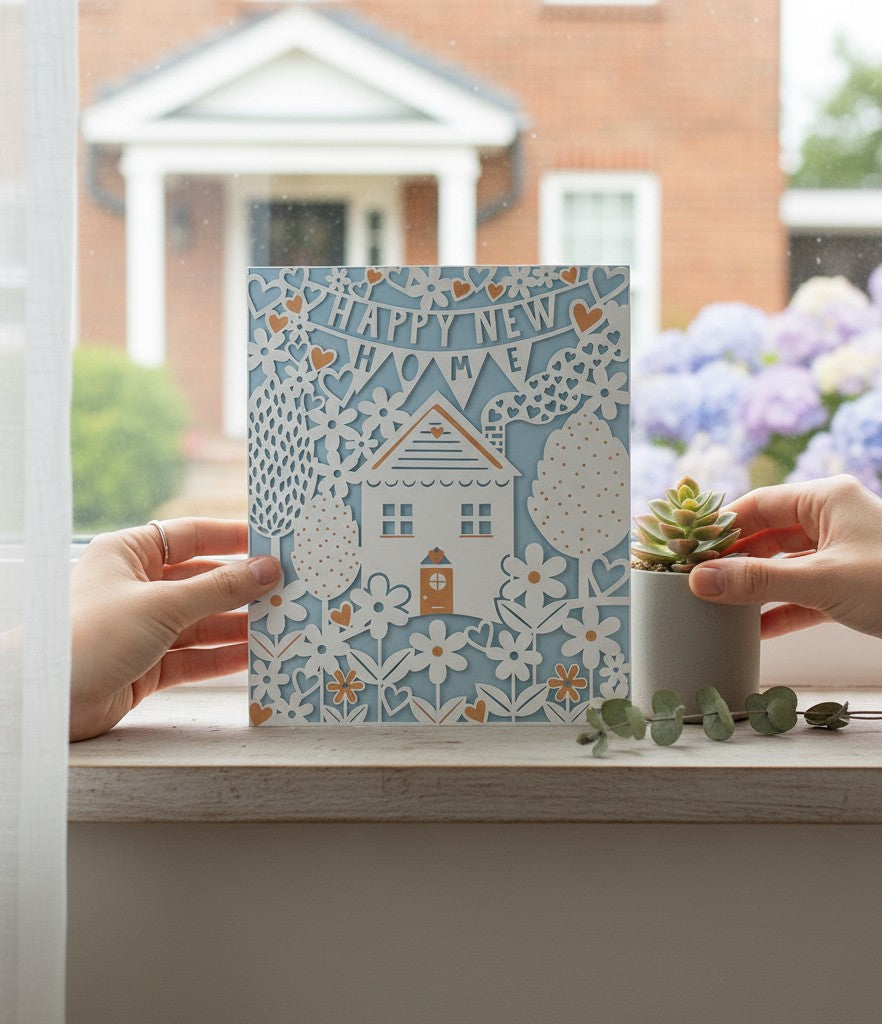 Made To Be Treasured laser cut card with "Happy New Home" banner, white house, flowers, and hearts.
